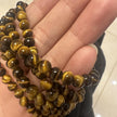Hand holding polished tiger eye beads, natural gemstone for protection and spiritual growth