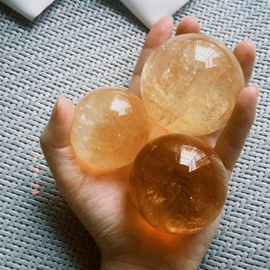 Hand holding three polished citrine crystal spheres for healing and spiritual growth