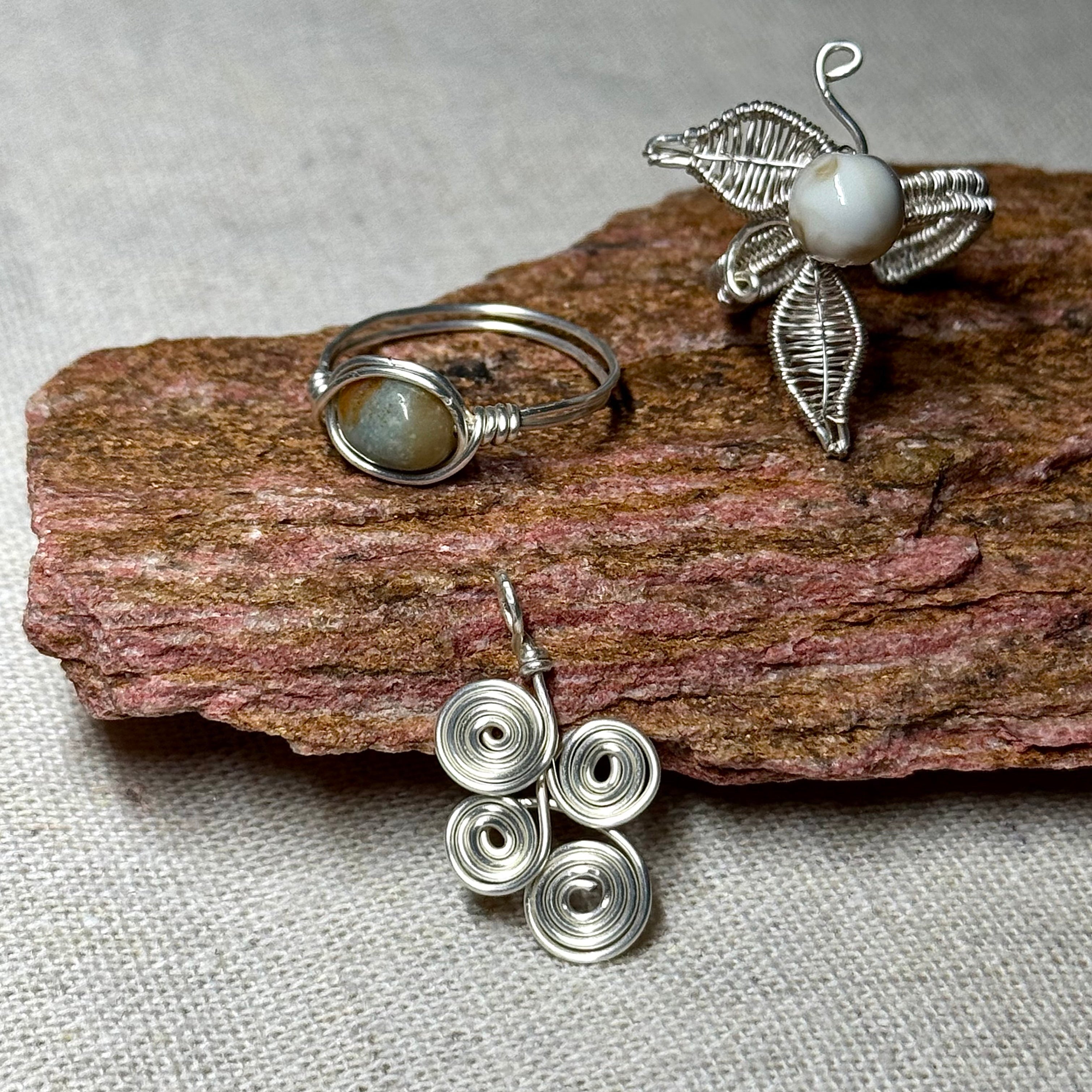 Handmade wire-wrapped gemstone jewelry set with crystal ring, leaf pendant, and spiral charm on natural stone