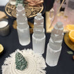 Selenite tower crystals for spiritual healing, protection, and anxiety relief, displayed with green crystal tree and ritual items.