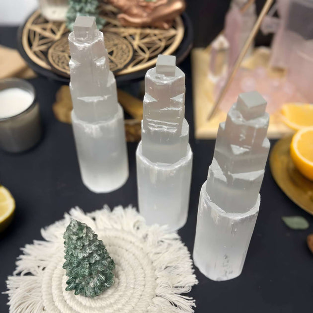 Selenite tower crystals for spiritual healing, protection, and anxiety relief, displayed with green crystal tree and ritual items.