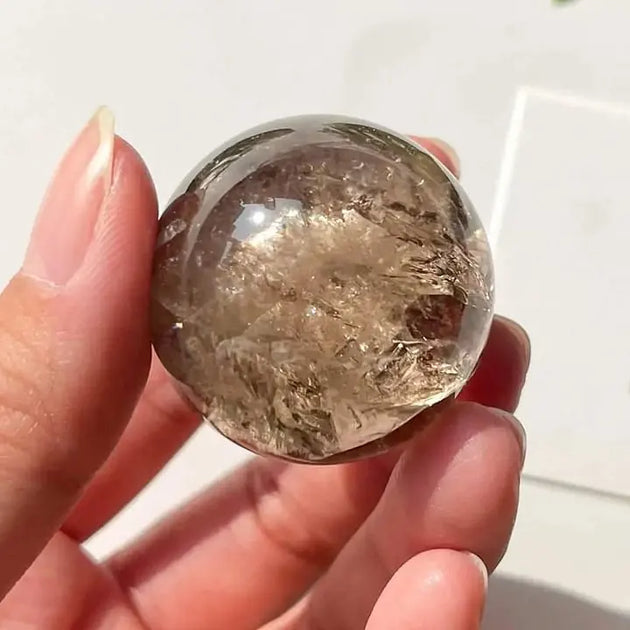 Hand holding a clear quartz sphere with internal inclusions, ideal for healing and spiritual growth.