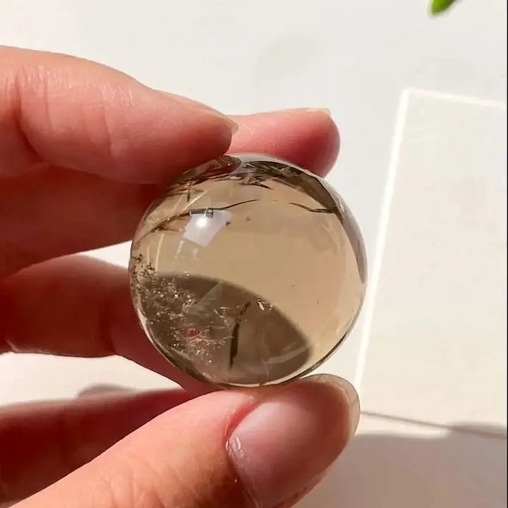 Hand holding a clear quartz sphere with natural inclusions, ideal for healing and spiritual growth.