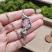 Handmade pink crystal pendant necklace with textured silver setting, held in hand against green moss background