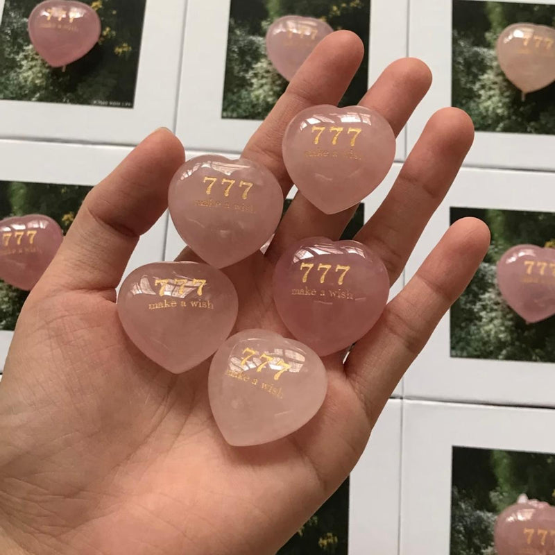 Hand holding pink heart-shaped rose quartz crystals engraved with 777 make a wish, spiritual healing stones