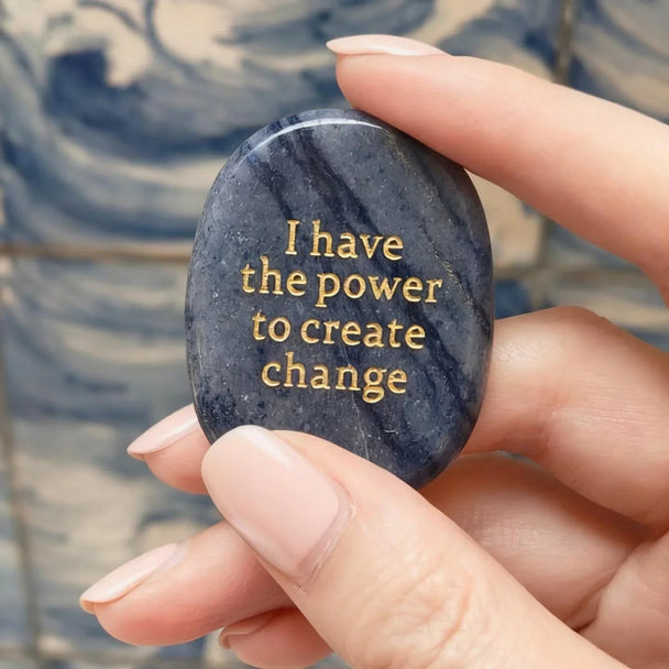 Hand holding dark blue affirmation stone with gold text 'I have the power to create change' for spiritual growth