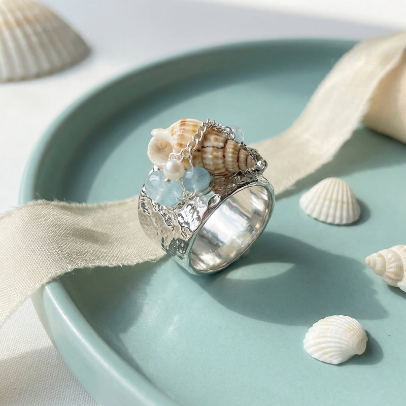 Handmade silver ring with seashell, aquamarine gemstones, and pearl, styled with sea-themed decor for spiritual jewelry lovers