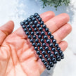 Hand holding black onyx beaded bracelet for protection and grounding, ideal for chakra healing and spiritual wellness.