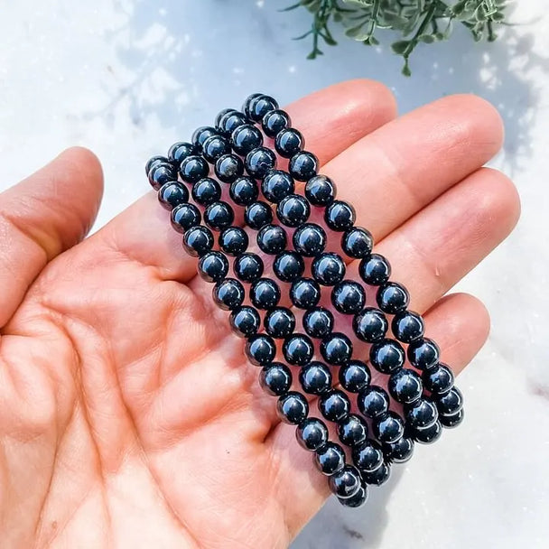 Hand holding black onyx beaded bracelet for protection and grounding, ideal for chakra healing and spiritual wellness.
