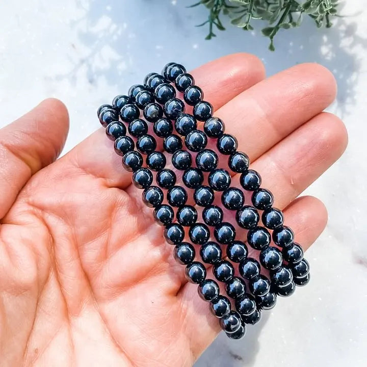 Hand holding black onyx beaded bracelet for protection and grounding, ideal for chakra healing and spiritual wellness.