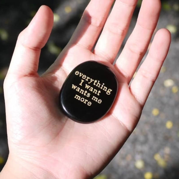 Hand holding black engraved stone with 'everything I want wants me more' for spiritual growth and manifestation
