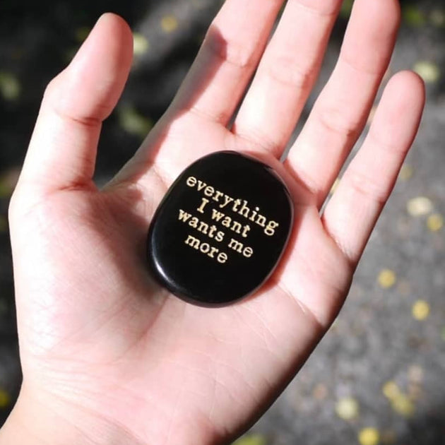 Hand holding black engraved stone with 'everything I want wants me more' for spiritual growth and manifestation