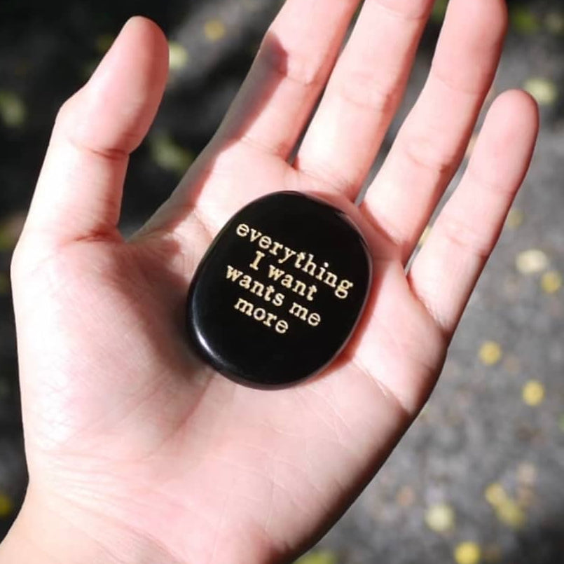 Hand holding black engraved stone with 'everything I want wants me more' for spiritual growth and manifestation
