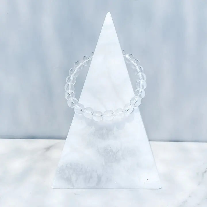 Clear quartz crystal bracelet on white marble pyramid, ideal for spiritual healing and chakra balance