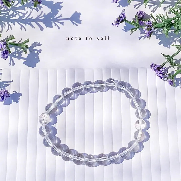 Clear quartz crystal bracelet for spiritual growth, surrounded by lavender flowers on white ridged surface