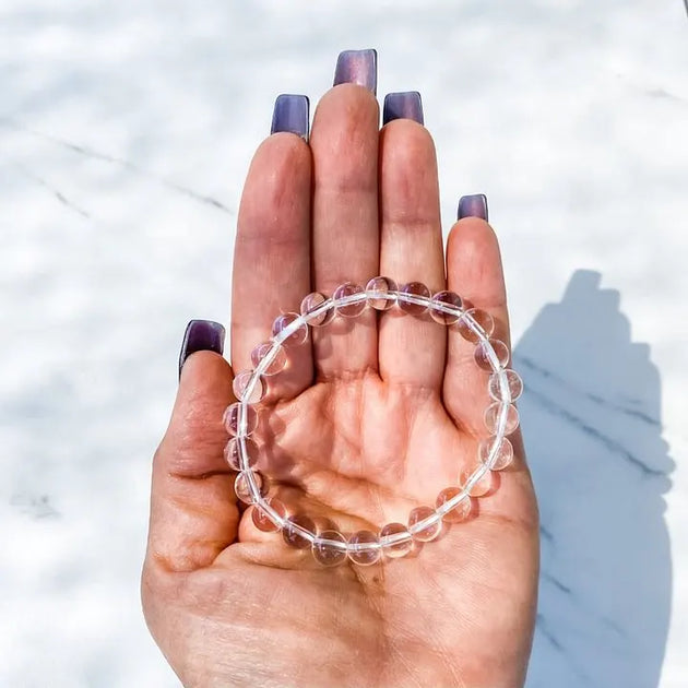 Clear quartz beaded bracelet for spiritual healing and chakra balance, held in hand over marble