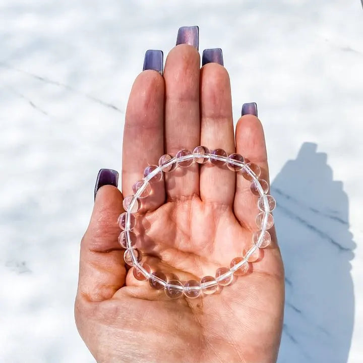 Clear quartz beaded bracelet for spiritual healing and chakra balance, held in hand over marble