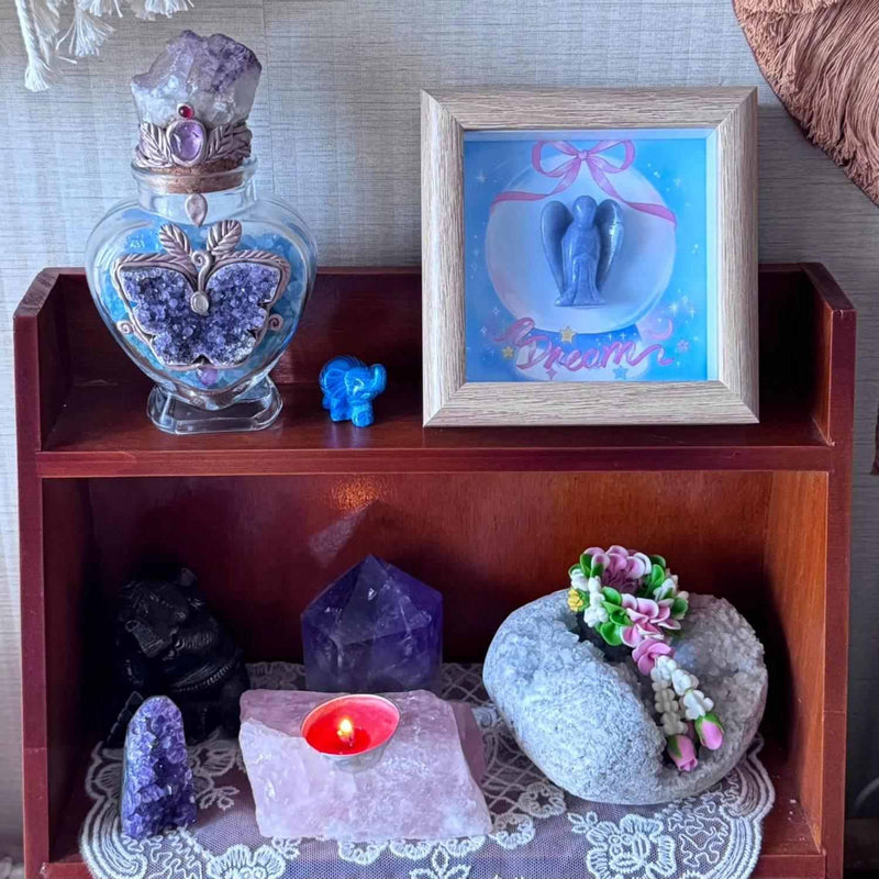Amethyst crystal decor with angel art, healing stones, and candle on wooden shelf for spiritual ambiance