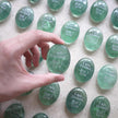 Hand holding green crystal stone engraved 'I am rooted But I flow' for spiritual grounding and mindfulness
