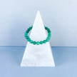 Green aventurine bracelet for healing and chakra balance, displayed on white marble pyramid stand
