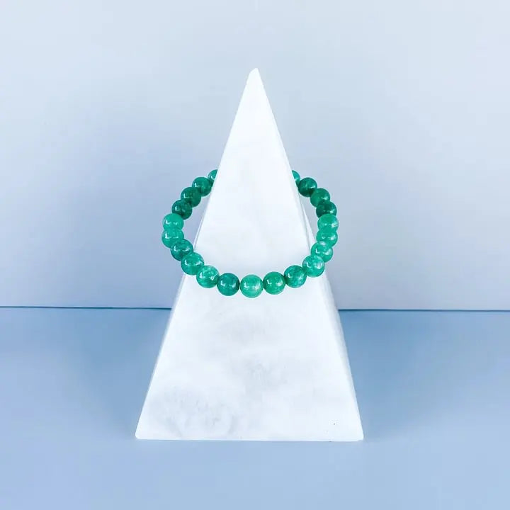 Green aventurine bracelet for healing and chakra balance, displayed on white marble pyramid stand