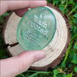 Hand holding green crystal with 'I am rooted but I flow' engraving, nature background for spiritual growth