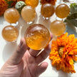 Hand holding a polished citrine crystal sphere with orange flowers, ideal for healing and spiritual growth