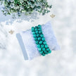 Malachite beaded bracelet on soft pillow, surrounded by greenery and gold accents for spiritual healing