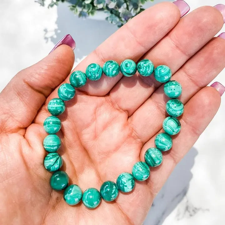 Hand holding green malachite beaded bracelet for healing and chakra balance