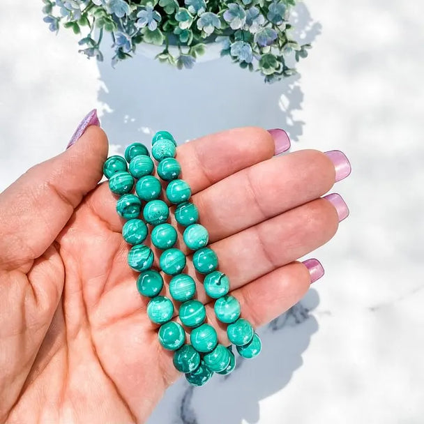 Hand holding vibrant green malachite beads for chakra healing and spiritual growth