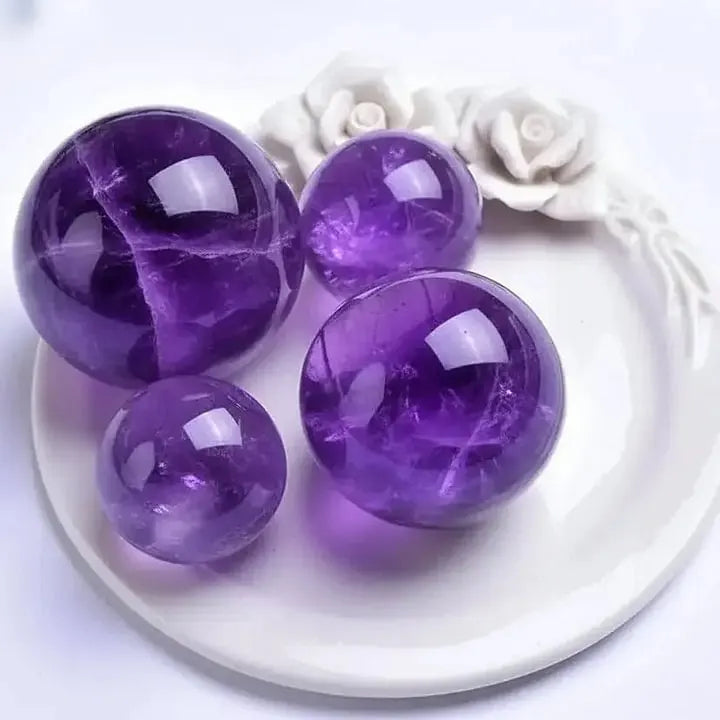 Polished amethyst spheres for spiritual healing and chakra balance, displayed on a white ceramic plate with floral details.