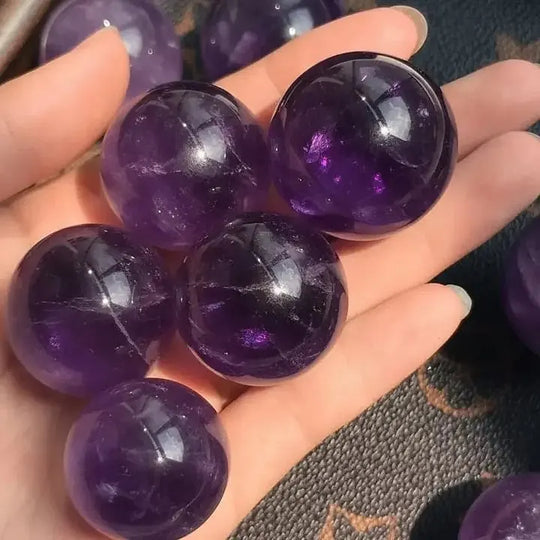 Hand holding polished amethyst spheres for spiritual healing and chakra balance