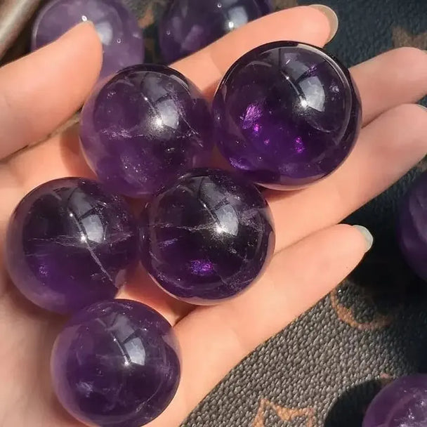Hand holding polished amethyst spheres for spiritual healing and chakra balance