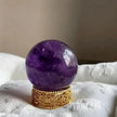 Polished amethyst crystal sphere on ornate gold stand for spiritual healing and chakra balance