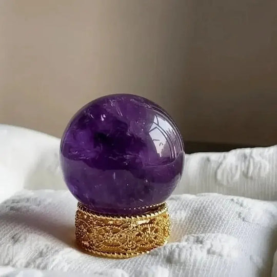 Polished amethyst crystal sphere on ornate gold stand for spiritual healing and chakra balance