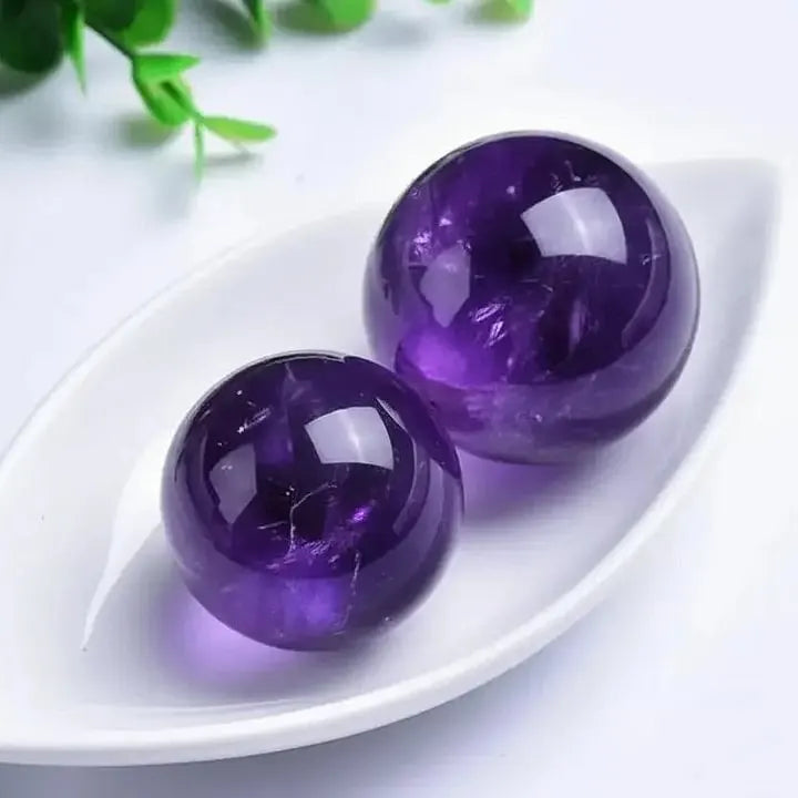 Two polished amethyst crystal spheres for spiritual healing and chakra balance, displayed on white dish with greenery.