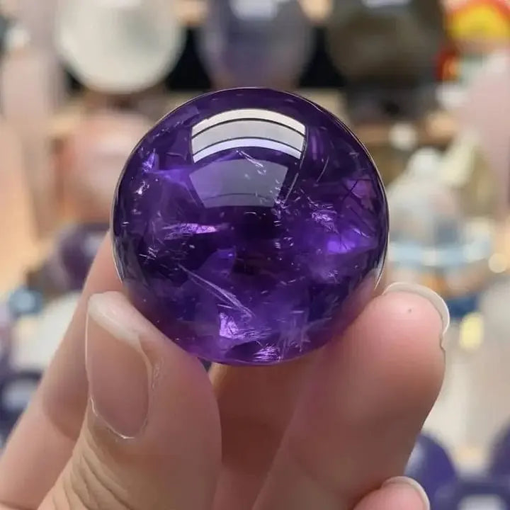 Hand holding polished amethyst crystal sphere for spiritual healing and chakra balance