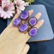 Hand holding five amethyst gemstone rings with gold settings and crystal accents, ideal for spiritual healing and chakra balance.