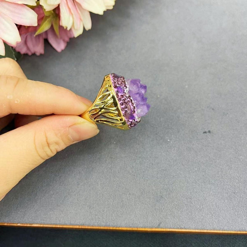 Hand holding amethyst crystal ring with gold band and purple gemstones, ideal for spiritual healing and chakra balance
