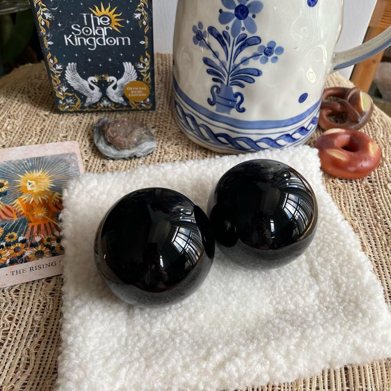 Two polished black obsidian spheres for spiritual healing and protection, displayed with tarot cards and crystals.