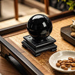 Polished black obsidian sphere on carved stand, ideal for protection and spiritual healing