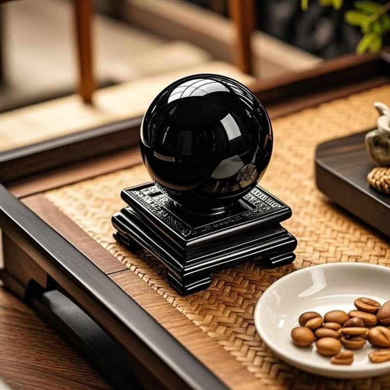 Polished black obsidian sphere on carved stand, ideal for protection and spiritual healing