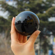 Hand holding polished black obsidian sphere for protection and spiritual growth, reflecting cityscape.