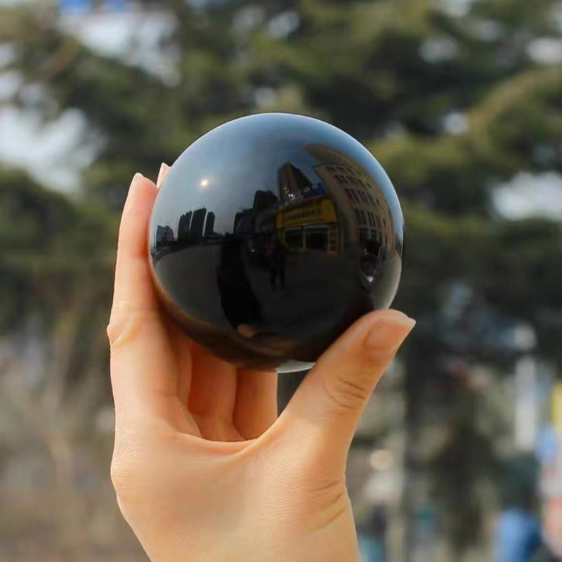 Hand holding polished black obsidian sphere for protection and spiritual growth, reflecting cityscape.