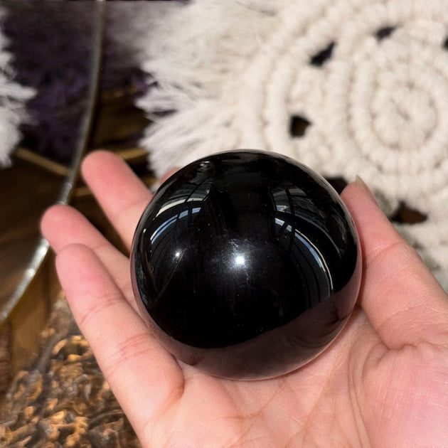 Hand holding polished black obsidian sphere for protection and spiritual grounding