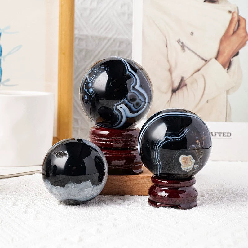 Polished black agate spheres with blue and white patterns, displayed on wooden stands for crystal healing and decor.