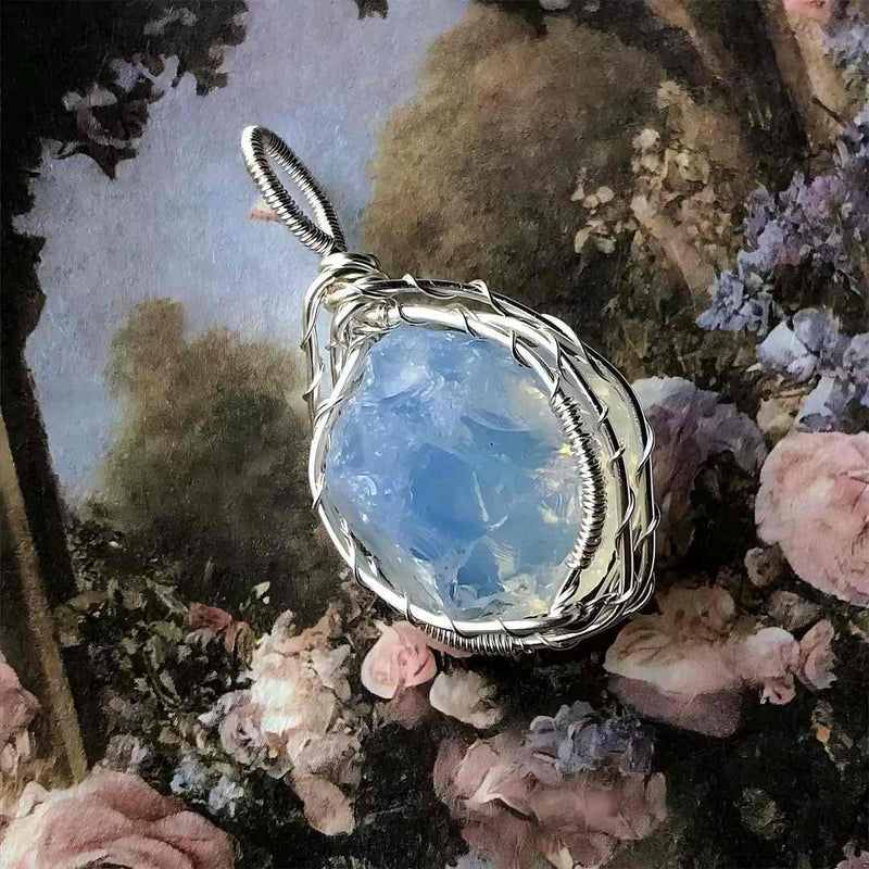 Handmade wire-wrapped moonstone pendant for spiritual healing and chakra balance, set against floral backdrop