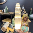 Glowing selenite tower lamp with Mother Earth statue, sage bundle, and spiritual decor for healing and protection.