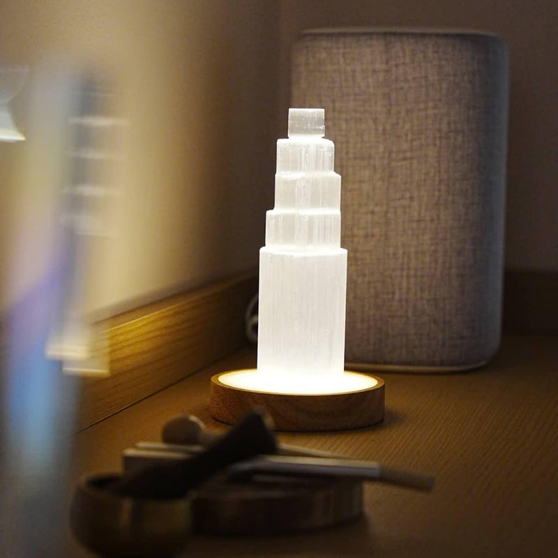 Glowing selenite tower lamp on wooden base, emitting soft light for serene ambiance and spiritual calm.