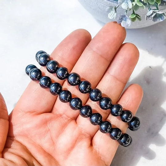 Hand holding black onyx beaded bracelet for protection and grounding, ideal for chakra healing and spiritual growth.
